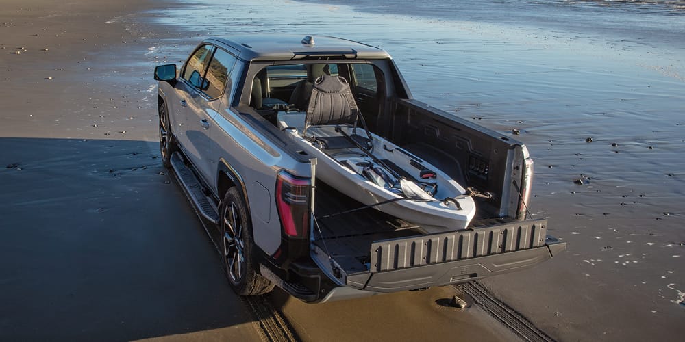 Sierra EV Denali parked on a beach with a canoe in the truck bed