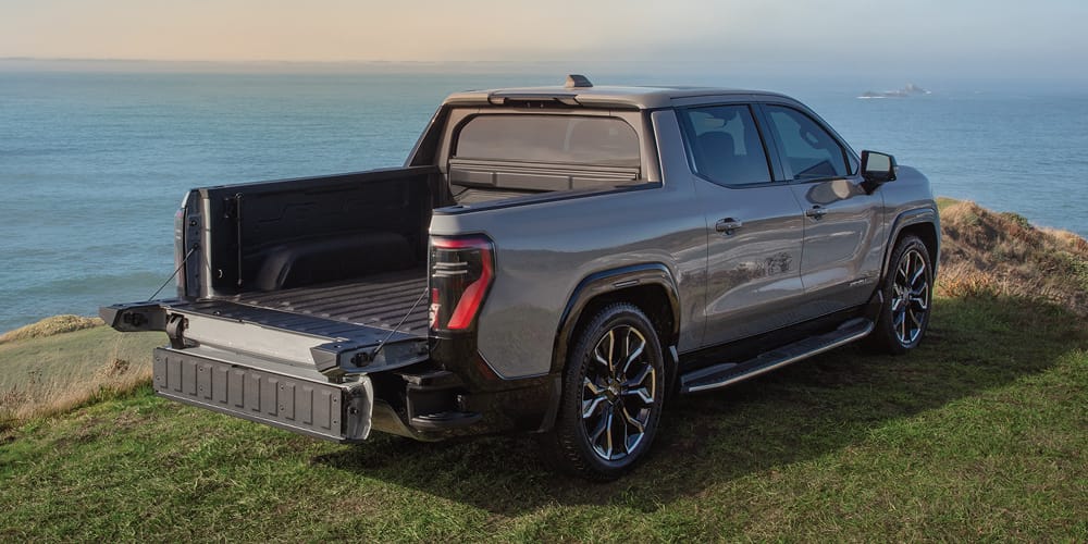 Sierra EV Denali parked on a hill overlooking an ocean with tailgate down